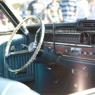 A photograph of an American Classic car, as seen through the side window, showing the steering wheel, dash board and blue interior, Image taken in August 2018 on a sunny day at Goodwood Motor Circuit, in the UK, at a classic car meeting (breakfast club), open to the general public.