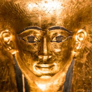 Gold-coloured replica model of an ancient Egyptian pharoah sarcophagus. Macro image studio shot. Horizontal colour image with copy space.