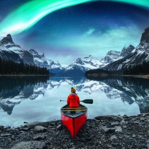 Traveler woman sitting on canoe with aurora borealis over Spirit Island in Maligne lake at Jasper national park, Alberta, Canada
